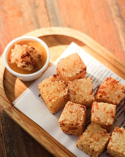 Golden fried tapioca cubes served with chilli jam, on a wooden board